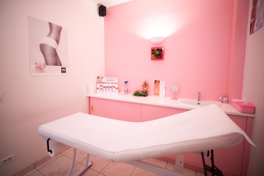 La cabine de soin du visage, aux murs roses, avec sa table de soin blanche